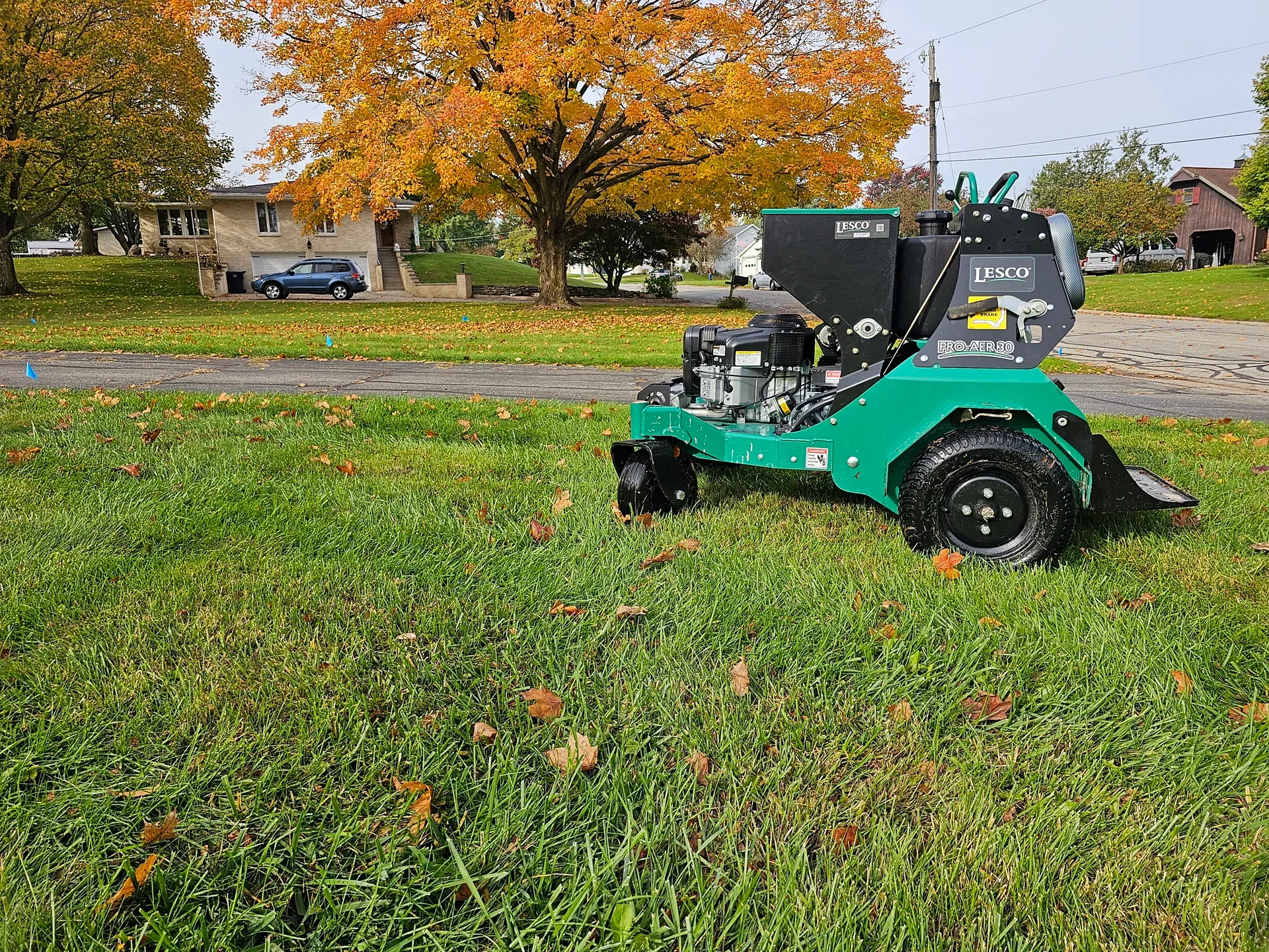 A parked Lesco Pro-Aer 30 core aerator on a lawn scattered with fall leaves