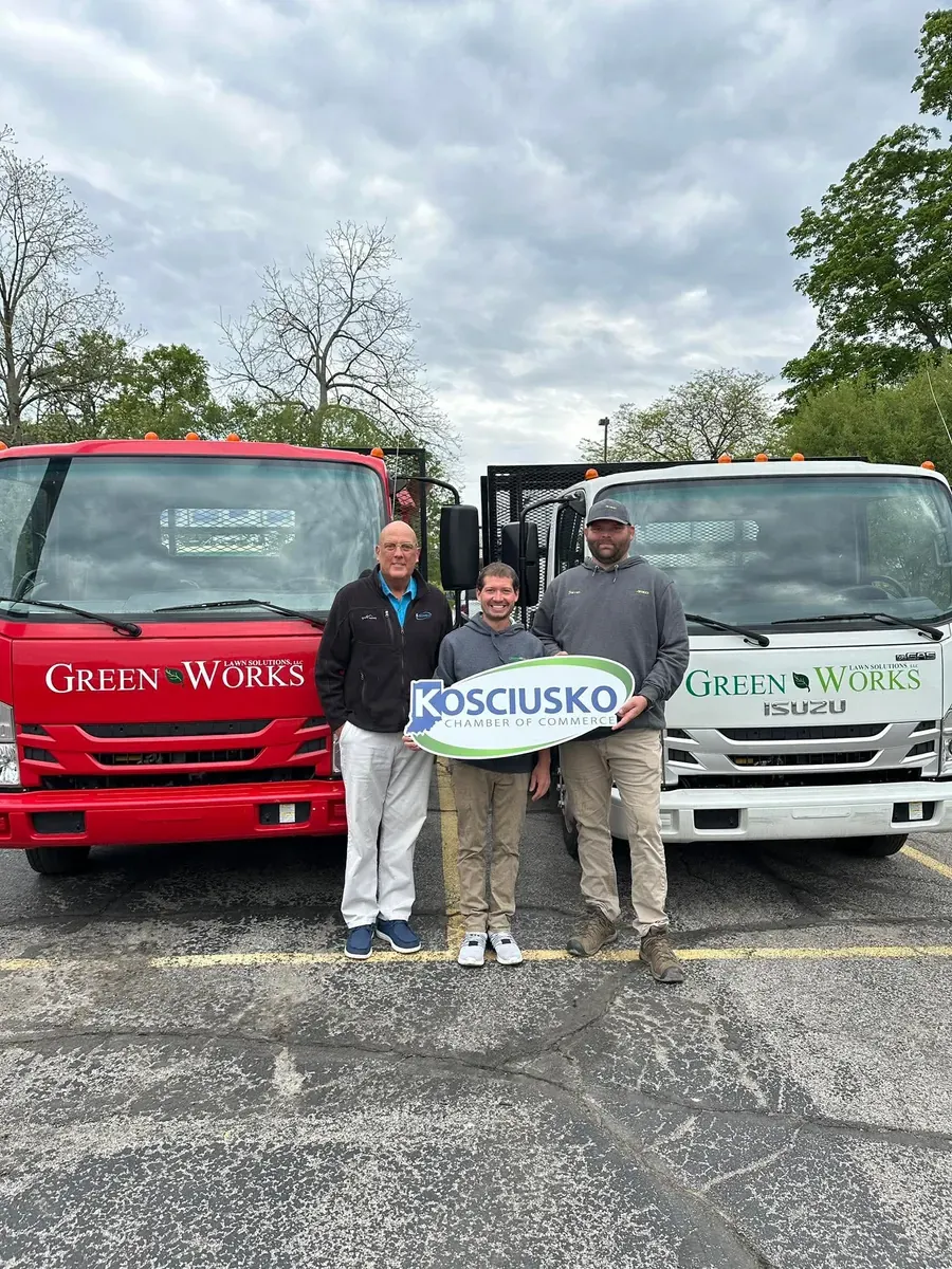 GreenWorks crew holding a Kosciusko Chamber of Commerce sign in front of two company trucks