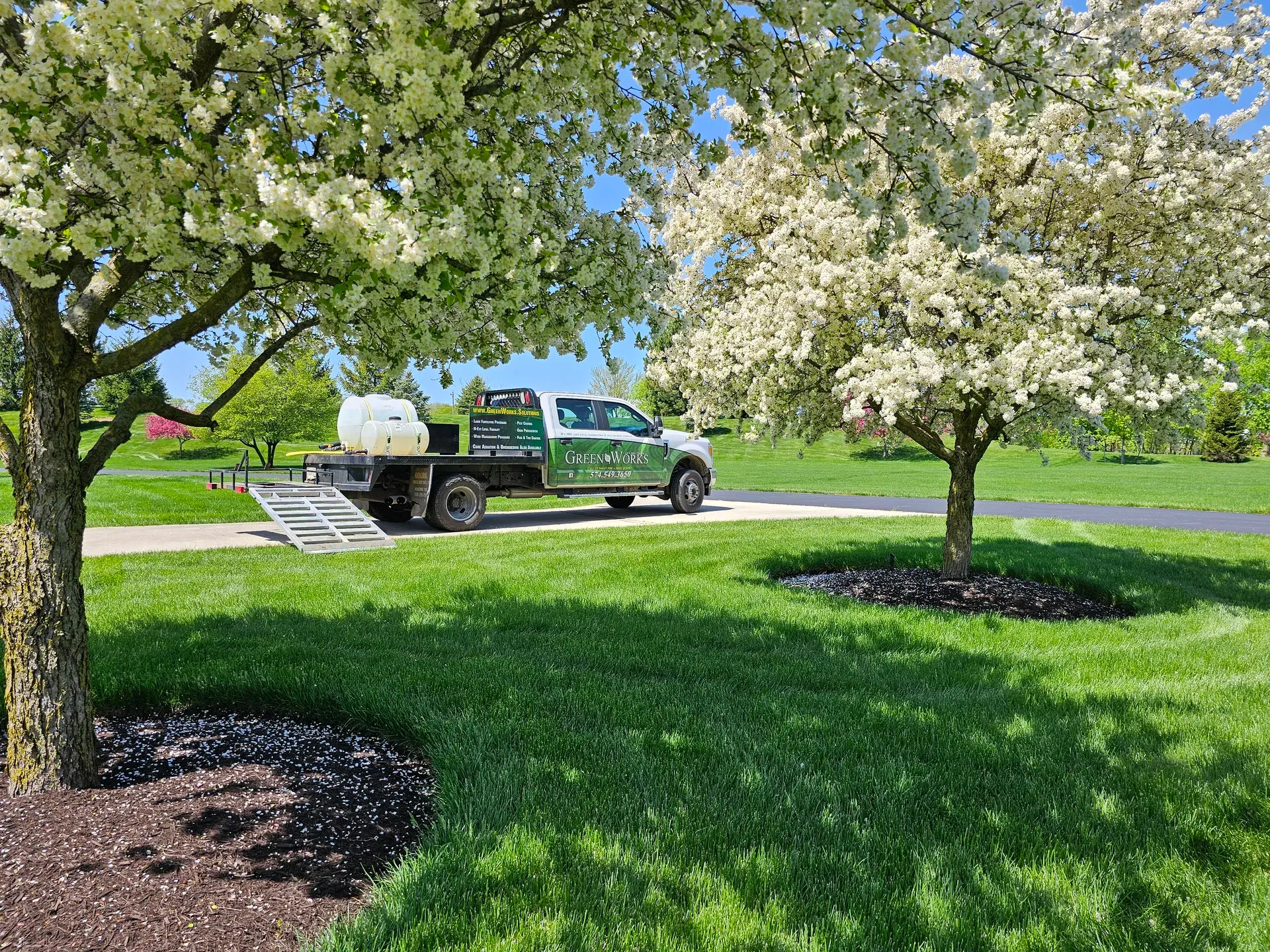 A GreenWorks truck parked beside a thick green lawn under blooming spring trees