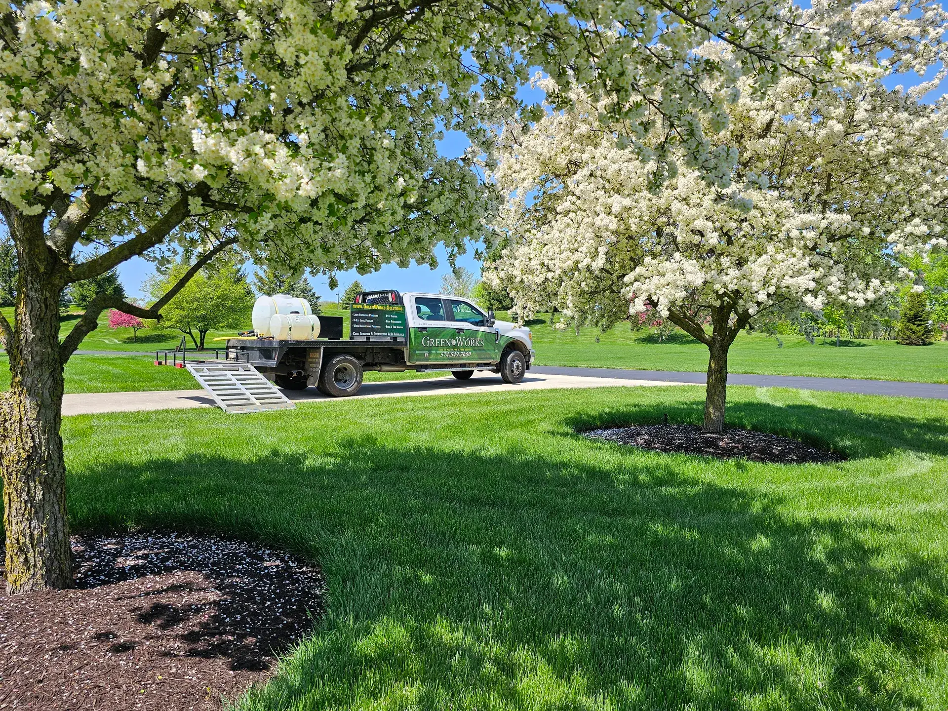 A GreenWorks truck parked beside a thick green lawn under blooming spring trees