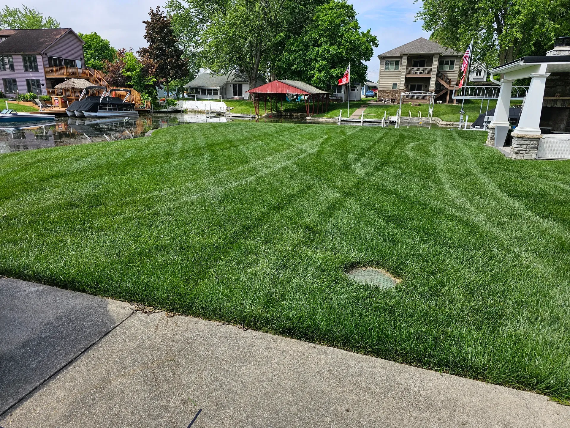 A diamond-striped lakeside lawn running down to the water, with docked boats behind