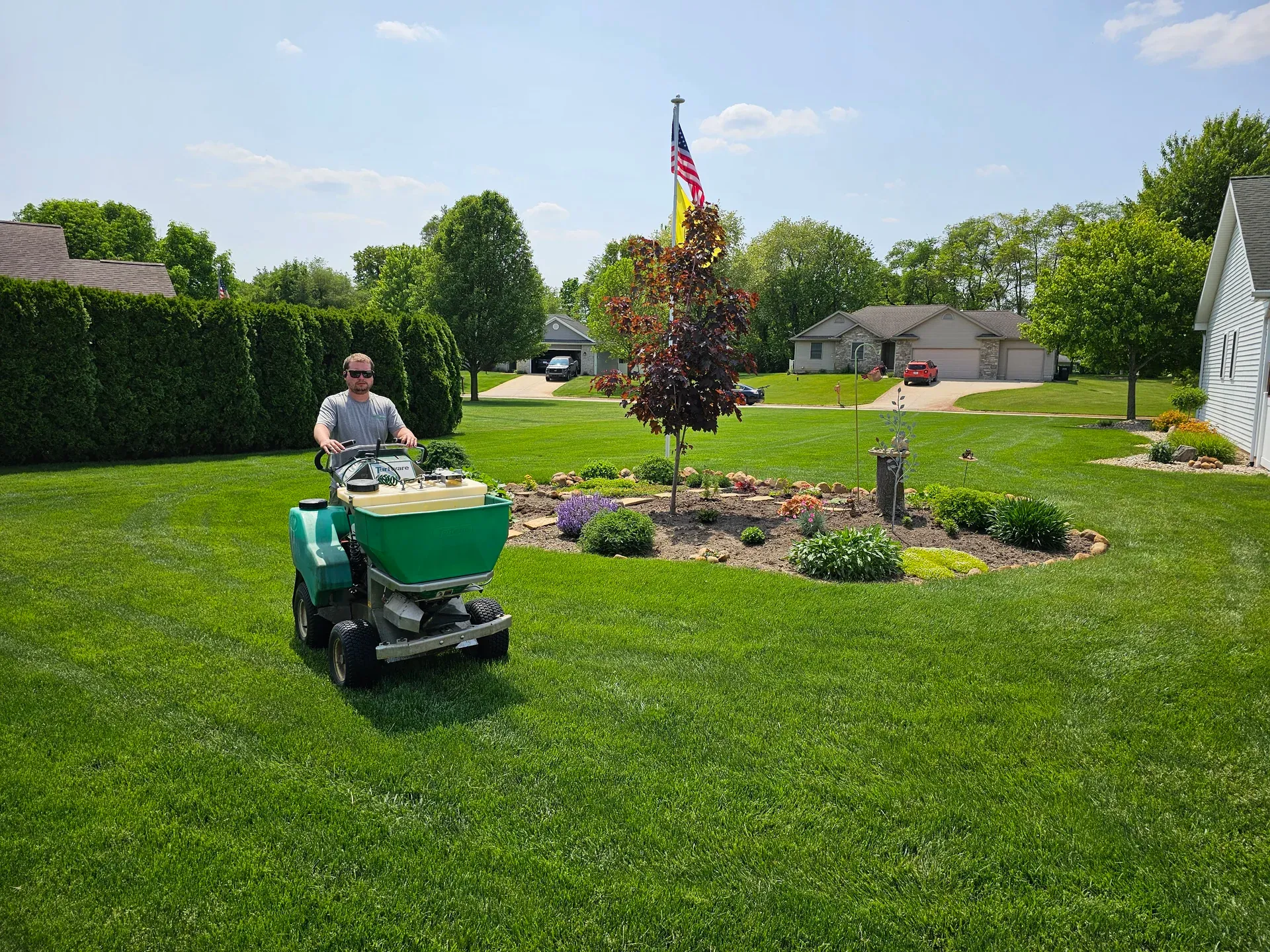 A GreenWorks technician walking a spreader across a treated front lawn